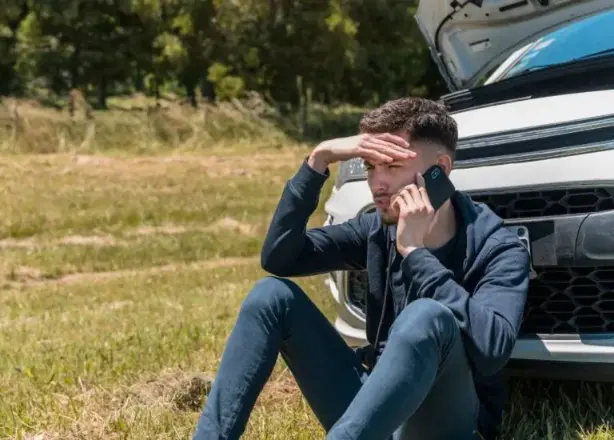 a man sitting on the ground with his head in the hood of a car